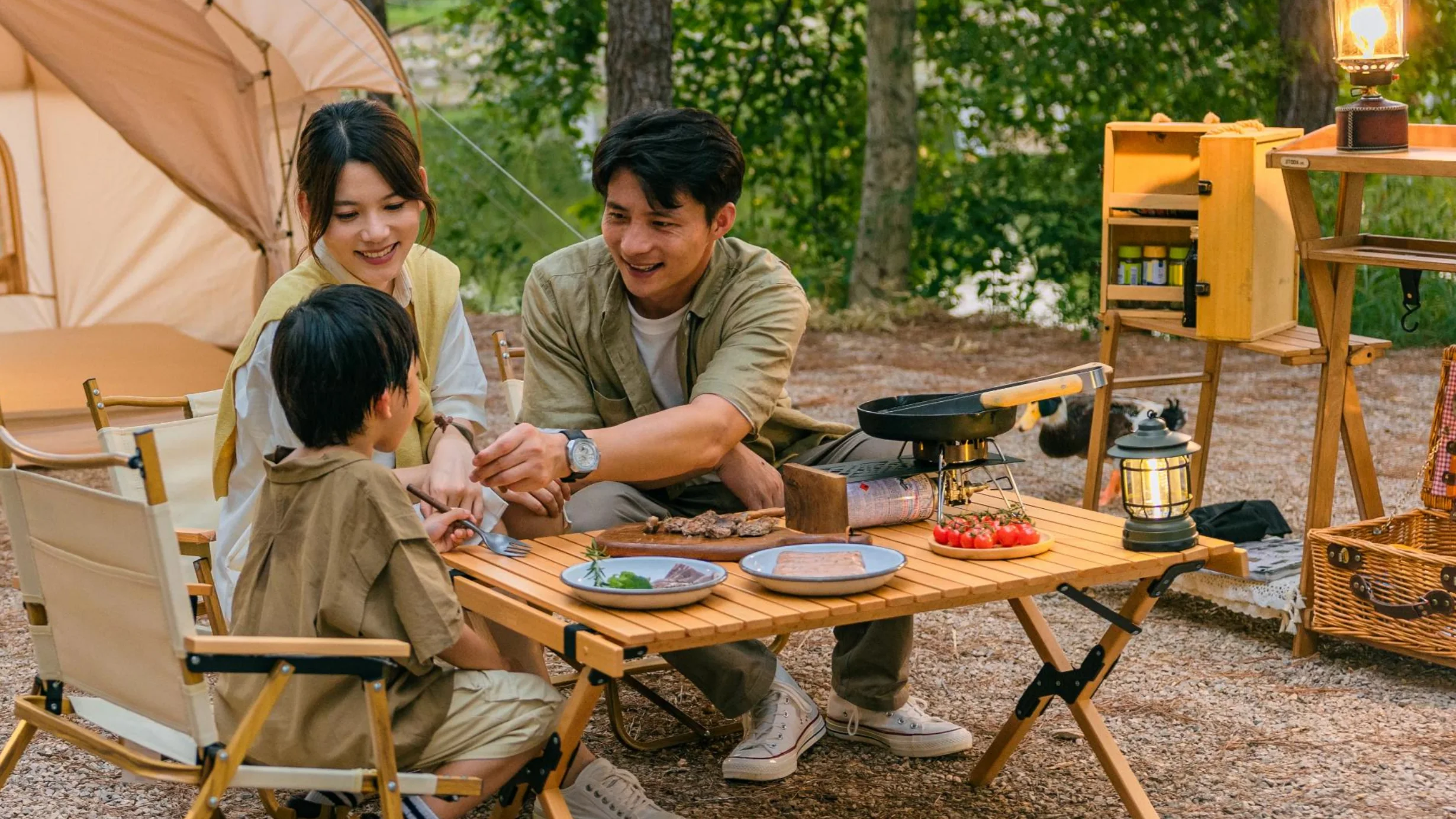 Family sharing a meal beside tents in a forest resort setting