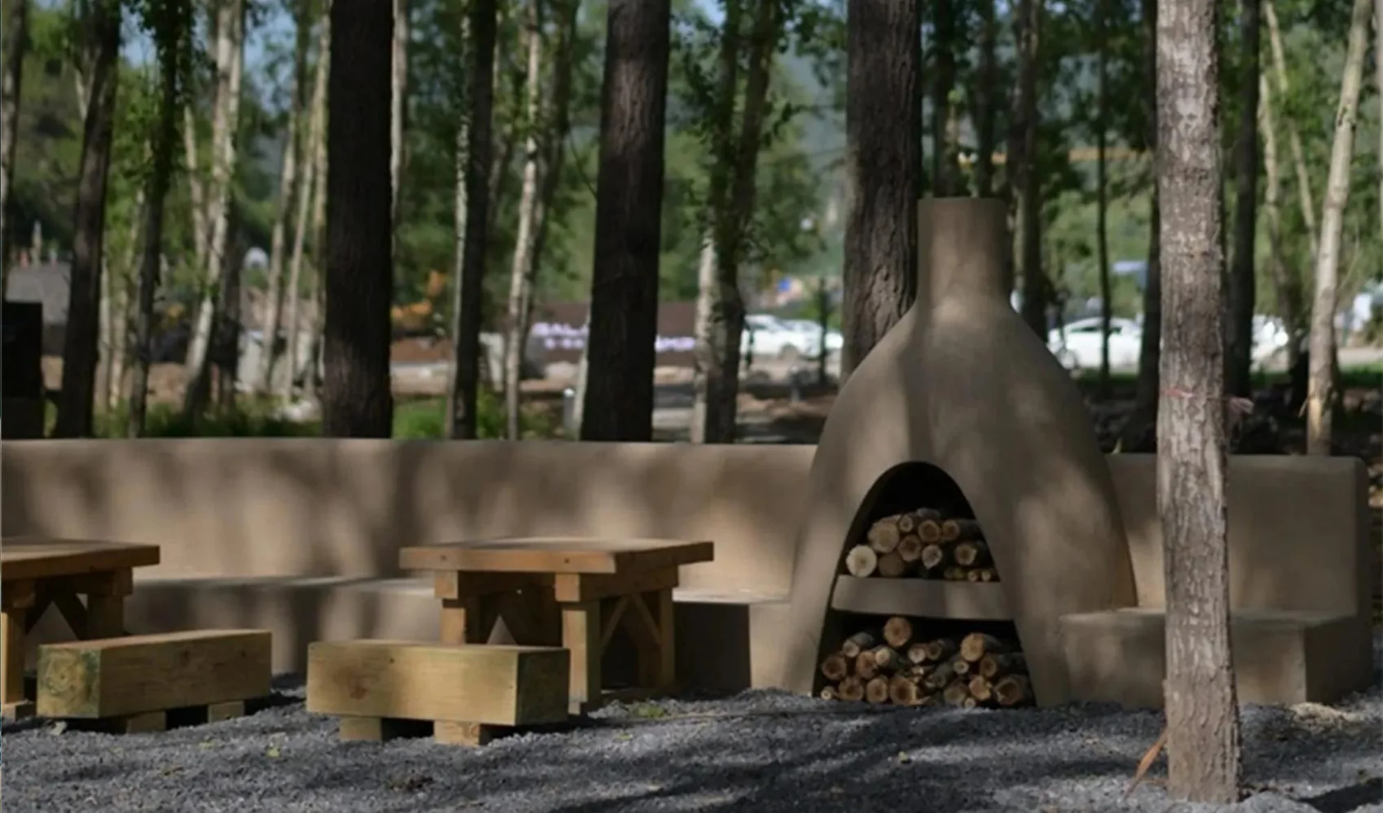 Outdoor dining area with shared tables and hearths among mature trees